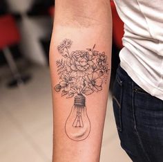 a person with a tattoo on their arm holding a light bulb and flowers in it