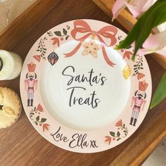 a plate with the words santa's treats on it next to some cookies and flowers