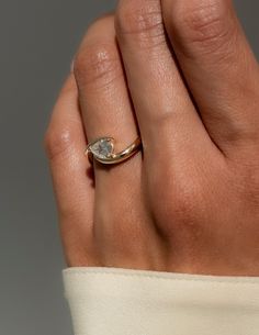 a woman's hand wearing a gold ring with a white diamond on it,