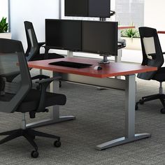 an office desk with two monitors on it and three chairs around it in front of a window