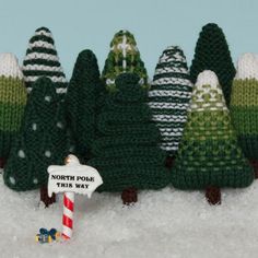 knitted christmas trees in the snow with a sign that says north pole this way