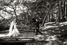 a bride and groom walking on a wooden deck in the woods at their wedding day