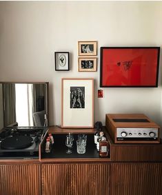 an old record player sits on top of a wooden cabinet in front of framed pictures