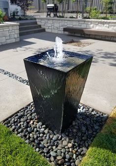 a water fountain sitting in the middle of a garden area with rocks and grass around it