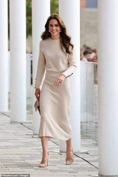 a woman in a beige dress is walking down the street with her hand on her hip