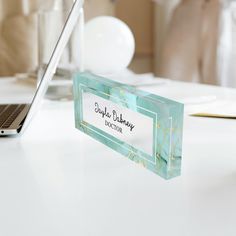 a desk with a laptop and a name plate on it, sitting next to a white table