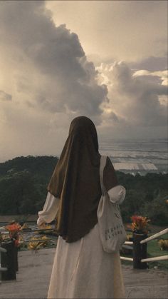 a woman in a brown and white dress is looking at the ocean with clouds above her