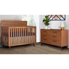 a baby crib next to a dresser with a potted plant on top of it