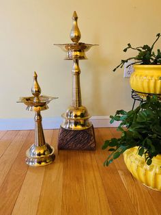 three gold colored candlesticks are sitting on a wood floor next to a potted plant