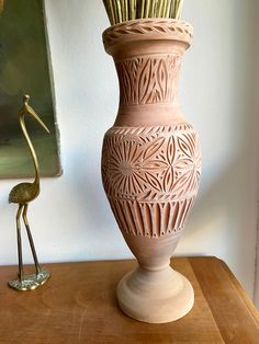 a tall vase sitting on top of a wooden table next to a small bird figurine