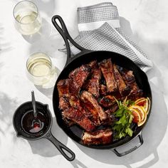 a pan filled with meat and vegetables next to glasses of wine