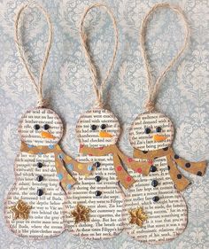 three snowmen made out of old book pages are hanging from twine strings on a wall