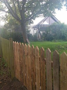 a wooden fence in front of a tree and some grass with a house in the background