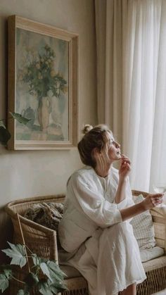 a woman sitting on top of a wicker couch next to a window