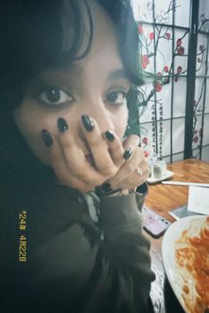 a woman with black nails covering her mouth and hand over her face while sitting at a table