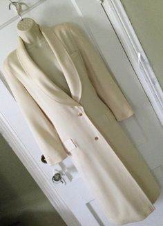 Ivory colored 2-button front 1990's vintage 3/4 length blazer/jacket, made in Franc, is by LOUIS FERAUD. This blazer/jacket is a 3/4 length, hitting mid-calf, is lined in silk, which has the 'Louis Feraud' name embossed all over the silk fabric (photo 6). The outer or shell fabric is a textured worsted wool (photo 7) Long shawl lapel, 2 goldtone buttons at the front placket for closure. Welt pocket at the right breast and 2 flap pockets at the right and left hip area. Long barrel sleeves, princess seams in the front and side back. The back has a decorative buttoned martingale band (photo 5). Coloring is a creamy ivory...like a vanilla. This long jacket/blazer was made in the 1990's in FRANCE. Size tag is missing; I estimated the size based on the measurements, to be a size 4. There's a tin Cream Double-breasted Long Coat, Button-up Beige Blazer, Double-breasted Cream Outerwear With Buttons, Cream Double-breasted Outerwear With Buttons, Cream Outerwear With Double Button Closure And Lapel Collar, Formal Long Coat In Winter White, Cream Long Outerwear For Daywear, Formal Winter White Long Coat, Formal Long Winter White Coat