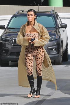 a woman in leopard print tights and boots walking down the street with a car behind her