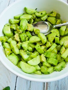 a white bowl filled with cucumbers on top of a wooden table next to a spoon