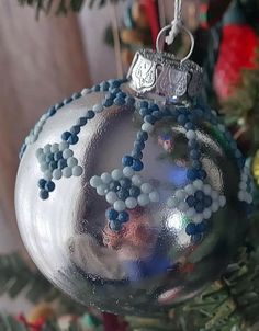 a silver ornament with blue and white beads on it hanging from a christmas tree