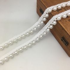 a white beaded ribbon with pearls on it next to a piece of wooden box