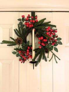 a christmas wreath hanging on the front door with a lit candle and evergreen leaves around it