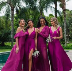 three women in purple dresses standing next to each other near a pool and palm trees