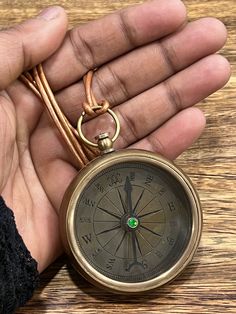 a person holding a compass in their hand on top of a wooden table next to a key chain