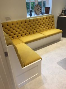 a yellow couch sitting in front of a window next to a white table with a clock on it