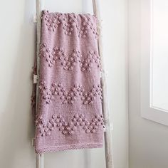 a pink crocheted blanket hanging on a ladder in a room with white walls