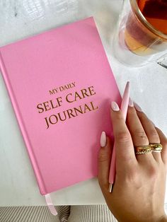 a woman's hand holding a pink notebook with the words, my daily self care journal