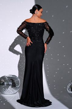 a woman standing in front of a disco ball wearing a black dress with sheer sleeves