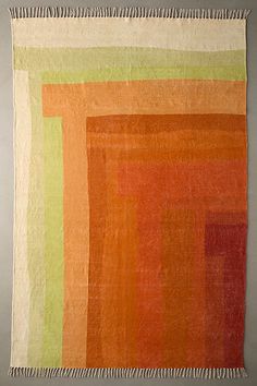 an orange, green and yellow rug with fringes on the bottom is shown in front of a gray wall