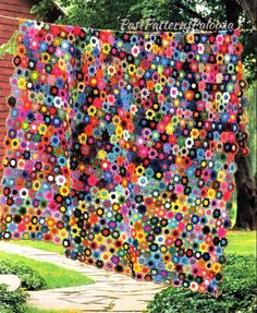 a large quilt hanging from the side of a building in front of a tree and grass area