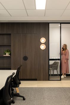 a woman standing in an office looking at her reflection in the glass door on the wall