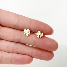 a hand holding a pair of gold earrings with leaves on the front and back of them