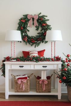 a christmas wreath is hanging on the wall above a white table with two baskets filled with candy canes