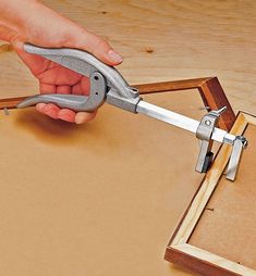 a person holding a pair of pliers over a piece of wood on top of a table