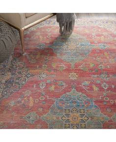 a red rug with an ornate design on the top and bottom, in front of a chair