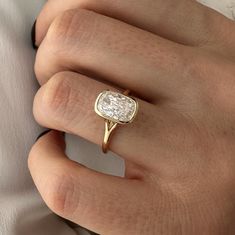 a woman's hand wearing a gold ring with a white diamond in the center