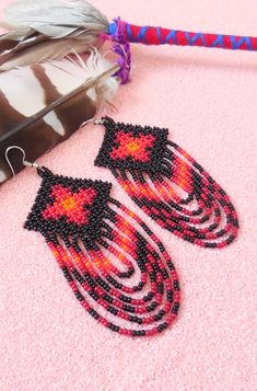 a pair of beaded earrings sitting on top of a pink surface next to a feather