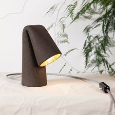 a lamp that is sitting on top of a white cloth covered tablecloth next to a potted plant