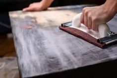 a person using a dust mop on top of a wooden table while someone is cleaning it