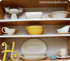 an open cabinet with dishes and cups on the top, in front of it is a yellow bird figurine