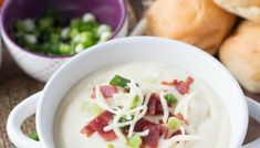 a white bowl filled with soup next to rolls