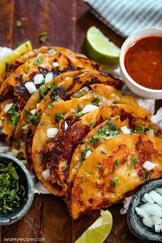 mexican food is served on a wooden table with limes and salsa in small bowls