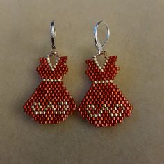 two pairs of red and silver beaded earrings on a white surface with one wearing a dress