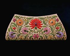 an embroidered purse with flowers and leaves on the front, sitting on a black background