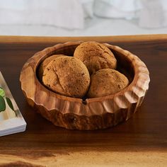 a wooden bowl filled with muffins next to a book on top of a table