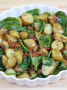 spinach and potato salad with bacon in a white bowl on a wooden table top