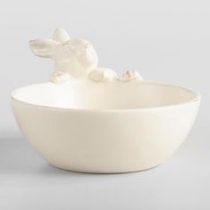 a white ceramic bowl with a rabbit figurine sitting in it's center